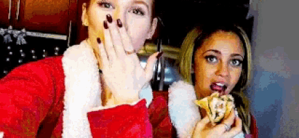 two women in santa claus costumes are taking a selfie and one is eating a donut .