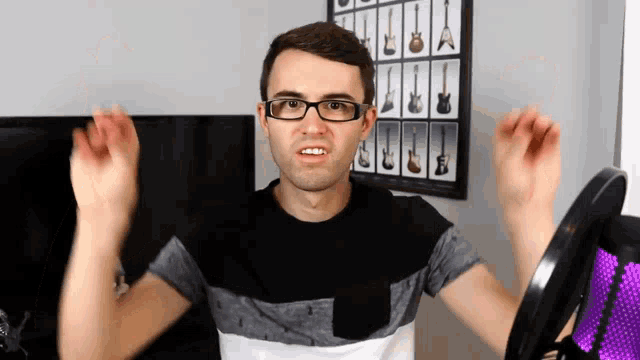 a man wearing glasses is standing in front of a guitar wall display