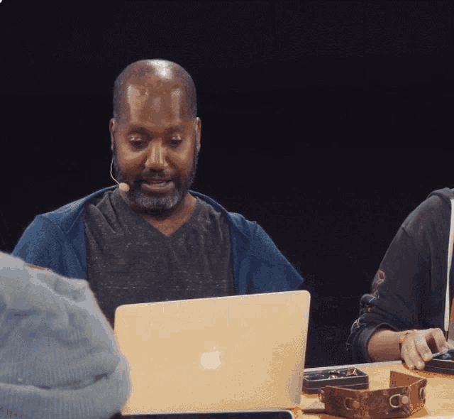 a man wearing a headset looks at an apple laptop