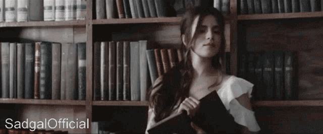 a woman standing in front of a bookshelf with sadgal official written on the bottom right