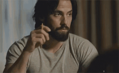 a man with a beard is smoking a cigarette while looking at himself in a mirror .