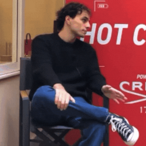 a man is sitting in front of a sign that says hot chicken
