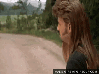a man with long hair and a mullet is standing on a dirt road ..