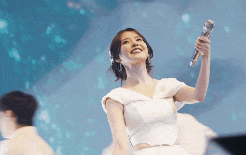 a woman in a white dress holds up a microphone