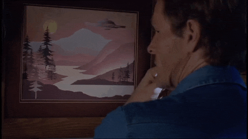 a man looks at a painting of a mountain and trees
