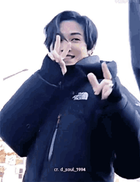 a man wearing a black jacket is giving a peace sign .
