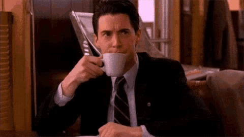 a man in a suit and tie is drinking from a cup while talking on a cell phone .
