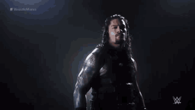a wrestler stands in front of a dark background with the words # wrestlemania on the bottom
