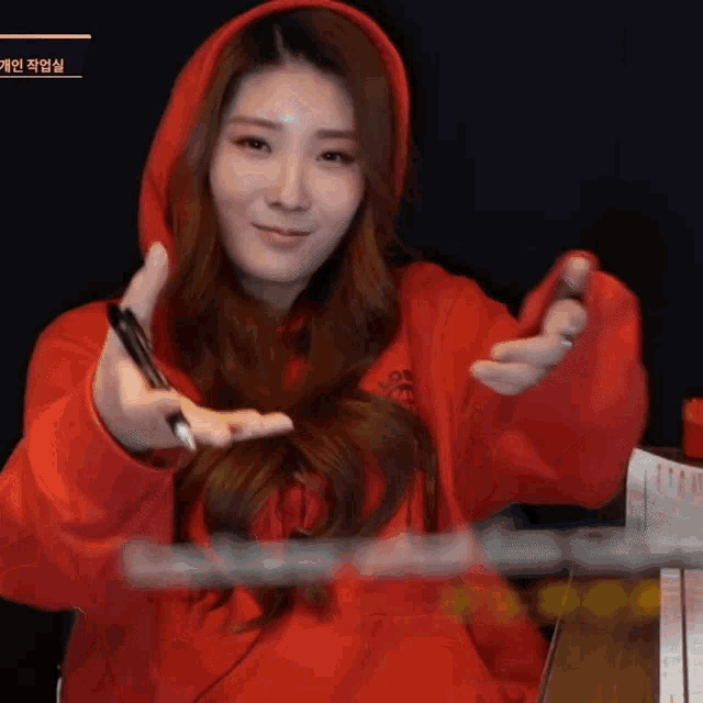 a woman wearing a red hoodie holds a pen in her hand
