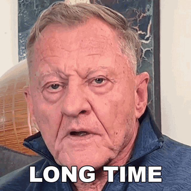 an older man is making a funny face and the words long time are on his face .