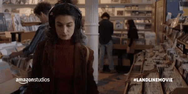 a woman is wearing headphones while standing in a record store .