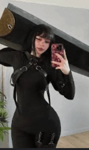 a woman in a black dress is taking a selfie with her phone while holding a large sword .