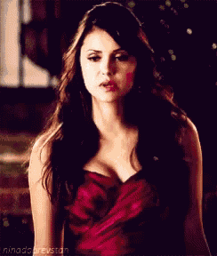 a woman in a red dress with a plunging neckline is standing in a dark room .