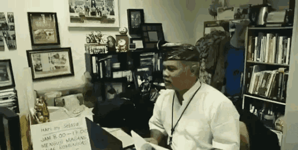a man in a white shirt is sitting at a desk with a sign on it that says happy 's sester