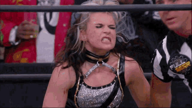 a female wrestler is standing in a ring with a referee behind her .