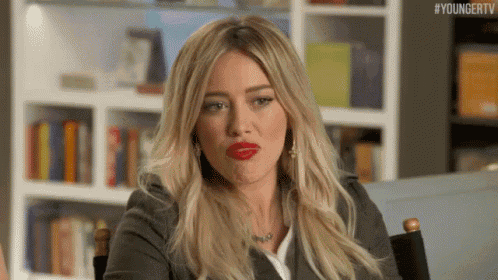 a woman with red lipstick is sitting in a chair in front of a bookshelf .
