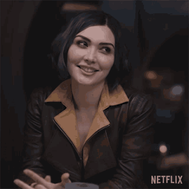 a woman in a brown leather jacket is smiling in front of a sign that says netflix