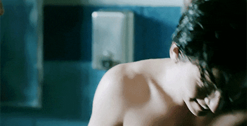 a shirtless man is sitting in a bathroom with his eyes closed and his mouth open .