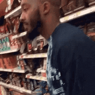 a man in a blue shirt is standing in a grocery store aisle .