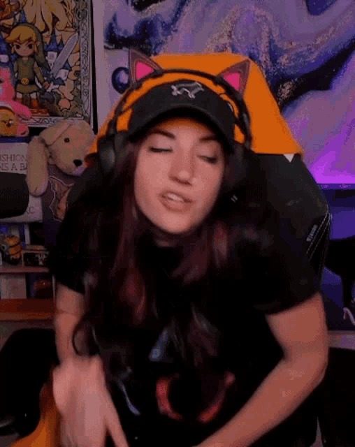 a woman wearing headphones and a hat with cat ears sits in a gaming chair