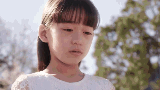 a little girl in a white lace dress looks sad