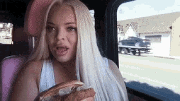 a woman is sitting in the back seat of a car holding a sandwich .