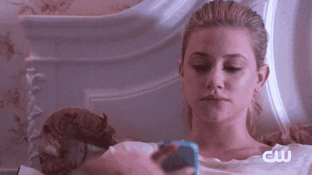 a woman is laying on a bed with a cat and looking at her phone .