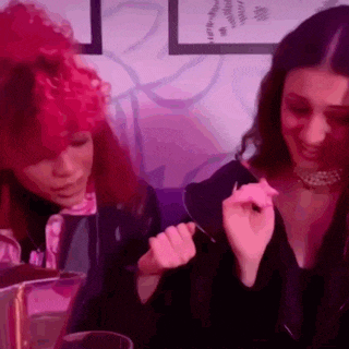 two women are sitting next to each other in a room with purple lights . one of the women has red hair .