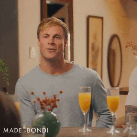 a man sitting at a table with glasses of orange juice and made in bondi on the bottom