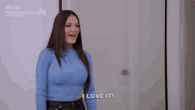 a woman in a blue sweater is standing in front of a door and says i love it .