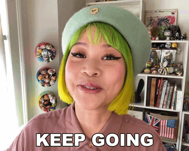a woman with green hair says keep going in front of a bookshelf