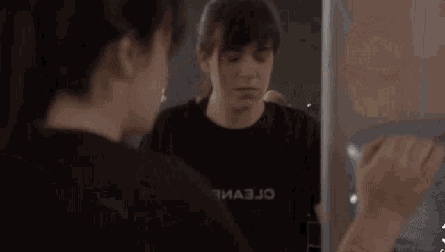 a woman is brushing her teeth in front of a mirror while wearing a black shirt that says r3ma3jo