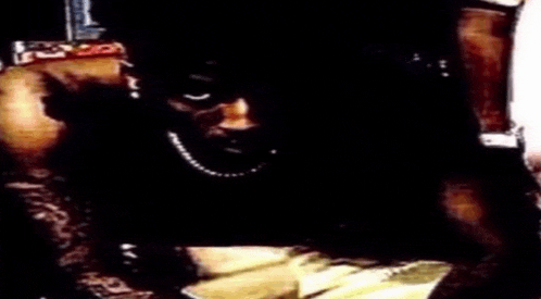 a man wearing a pearl necklace is sitting at a table with a plate of food in front of him .