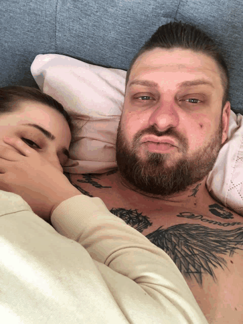 a man with a tattoo on his chest laying next to a woman with her hand on his face