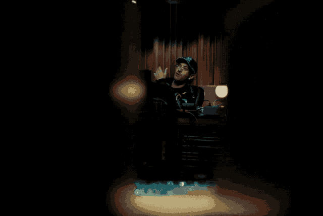 a man wearing a black shirt with the letter c on it stands in a dark room
