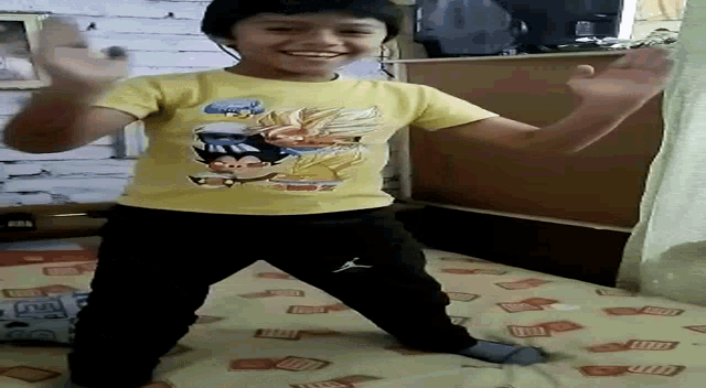 a young boy wearing a yellow shirt with a dragon ball z logo on it is dancing on a bed .