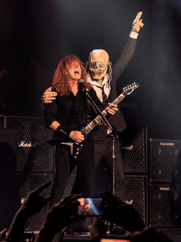 a man playing a guitar next to a skeleton with a marshall amp in the background