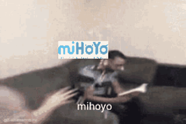 a man sitting on a couch with a mihoyo logo on his head