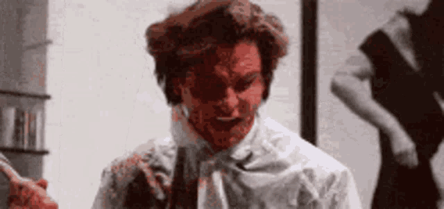 a man with blood on his face is standing in front of a woman in a black dress .