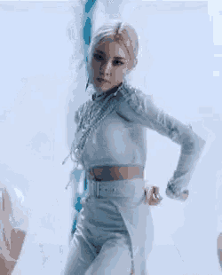 a woman in a white crop top and white pants is dancing in front of a window .