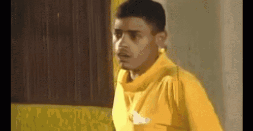 a man in a yellow shirt is standing in front of a window .