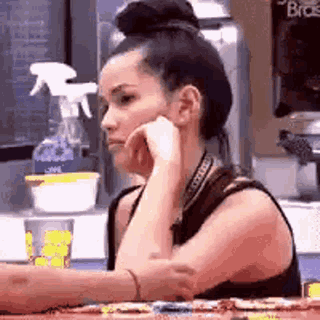 a woman is sitting at a table with her hand on her chin and a bun on her head .
