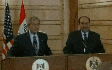 two men are standing at podiums with flags in the background and one of them has the letter m on his shirt