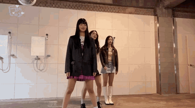 three girls are dancing in a room with white tiles and a mirror