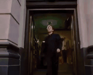 a man in a black shirt is walking out of a doorway .