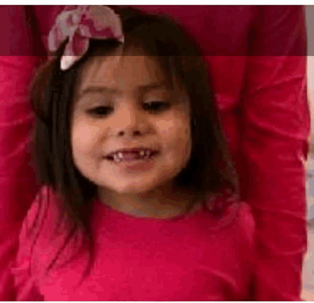 a little girl wearing a pink shirt and a pink bow in her hair is smiling .