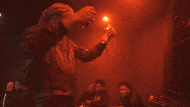a man in a black jacket stands in a dark room with red lights behind him