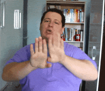 a man in a purple shirt making a stop sign with his hands