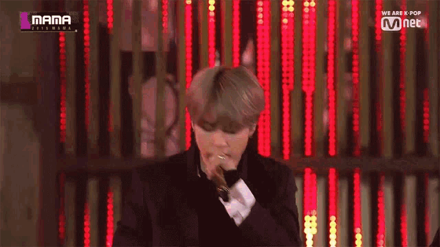 a man in a suit is singing into a microphone in front of a wall of lights
