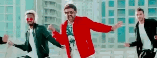 three men are dancing in front of a building in a video .